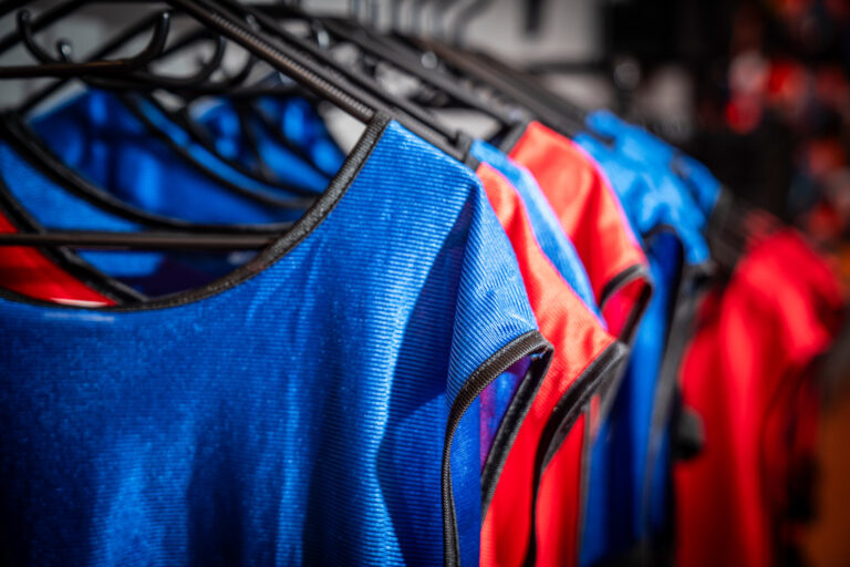Blaue und rote Teamvesten aufgehängt auf Kleiderbügeln.